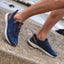 Reef Zuma navy sneakers, one facing left and one facing right, worn on a beachside walkway for everyday comfort