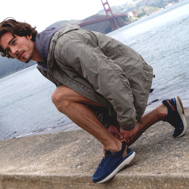 Reef Zuma blue sneakers facing left on a crouching man by the waterfront, with cushioned soles and breathable knit uppers