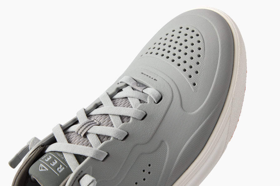 Close-up of grey sneaker facing upward and slightly left, showing breathable perforated upper and lightweight cushioned sole.