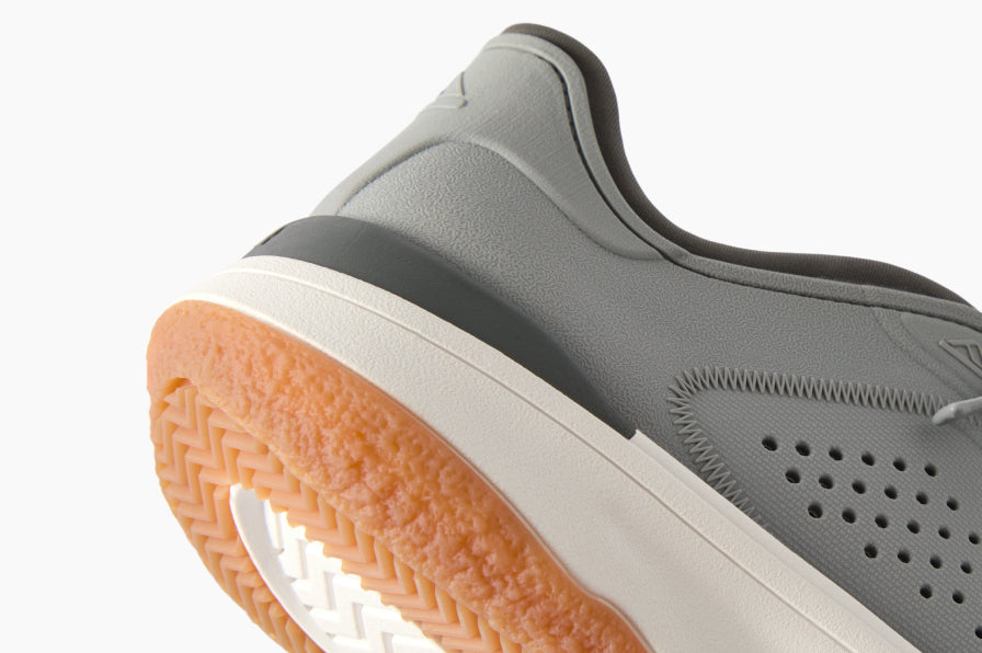 Close-up of the back heel and sole of a grey sneaker facing left, showing cushioned collar and textured gum outsole.