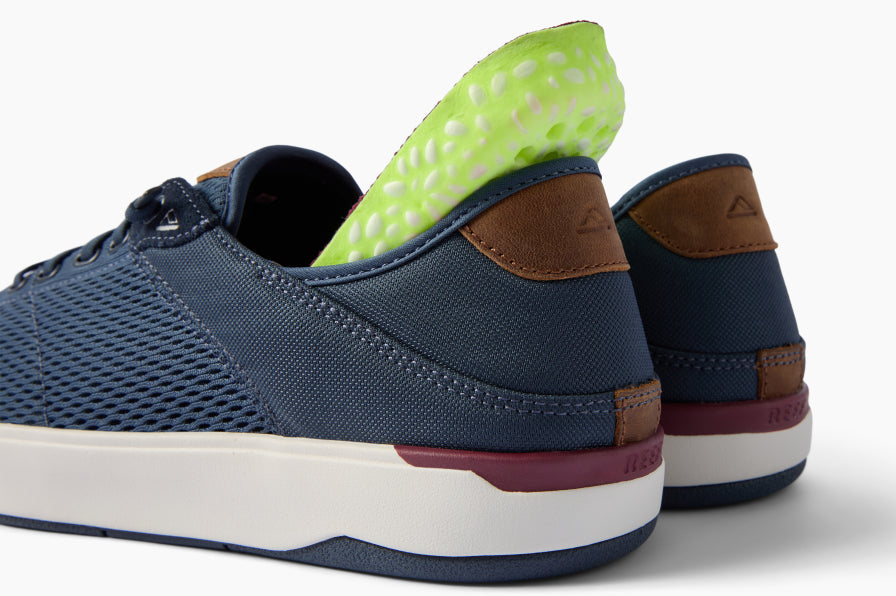 Navy sneakers facing left, rear three-quarter view with textured uppers, white midsoles, and a bright green insert