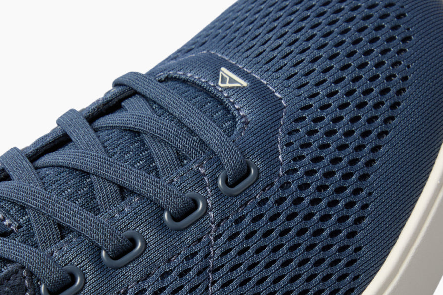 Close up of a navy sneaker facing right, showing the laces, breathable mesh upper, and cushioned sole edge