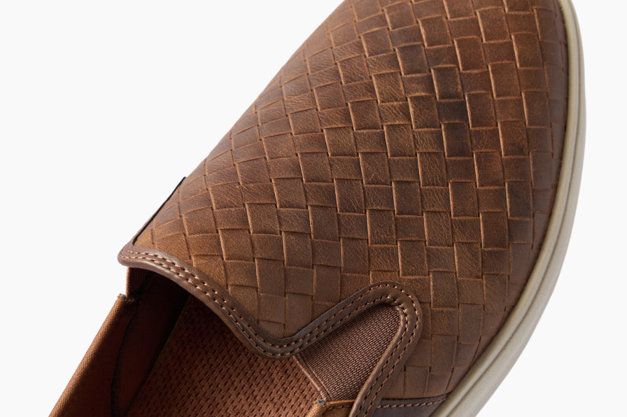 Close up of a brown woven shoe toe facing upper right with stitched detailing and textured lining