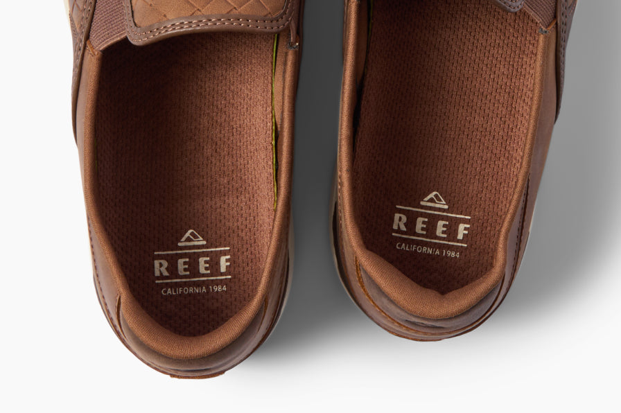 Top-down close-up of brown REEF shoes facing upward, showing textured insoles, rounded heels, and logo details
