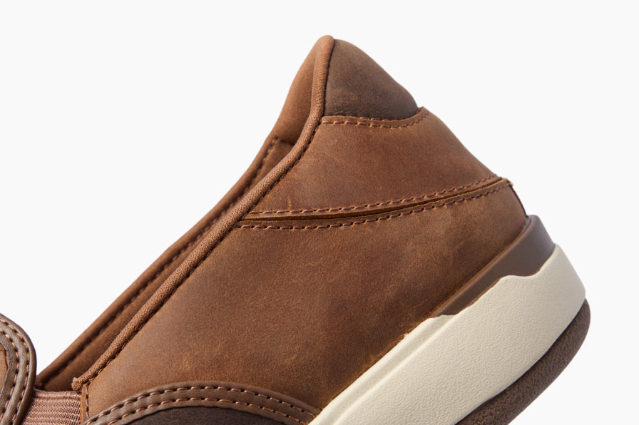 Close-up of a brown shoe facing left, showing its stitched upper and cushioned layered sole