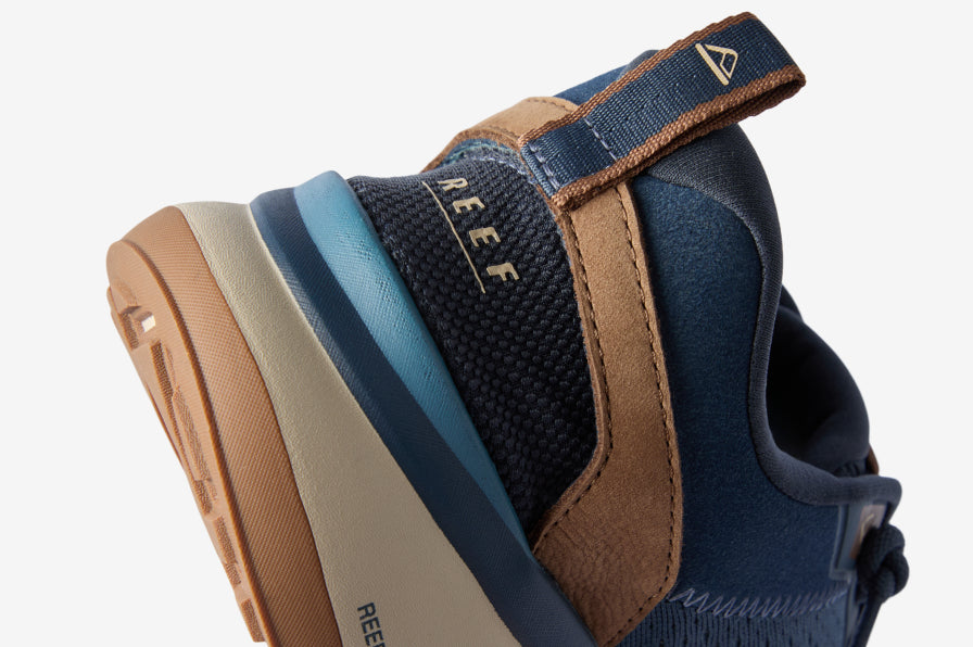 Close-up of a navy REEF shoe facing left, showing the cushioned heel, ankle strap, and textured outsole