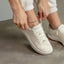 Reef Del Mar cream sneaker facing lower left with a woman tying the laces for comfortable everyday wear