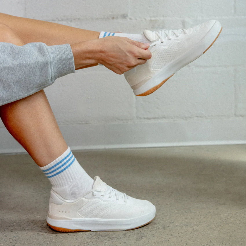 Person wearing white Reef Del Mar sneaker facing right, showcasing lightweight design and cushioned sole for all-day comfort.