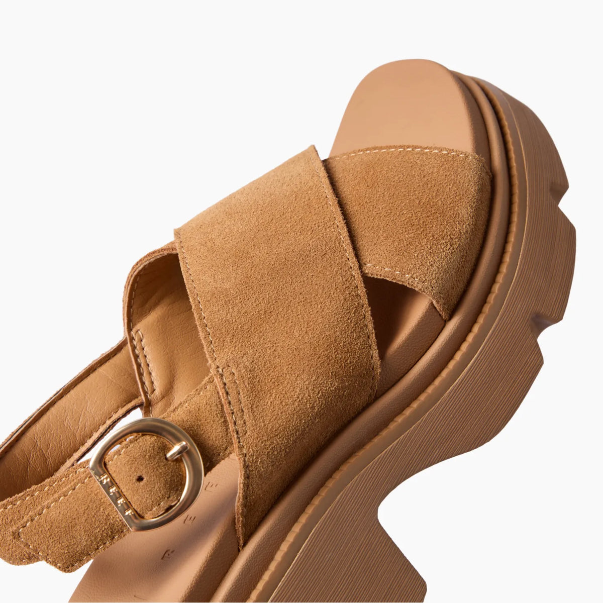 Close-up of a tan platform sandal facing upper right, with wide straps, metal buckle, and a ridged sole