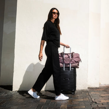 Neptune 2 white sneakers facing right as a traveler walks with luggage
