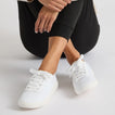 REEF Neptune 2 white sneakers facing forward on a seated model in black leggings