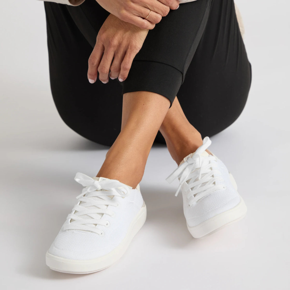 REEF Neptune 2 white sneakers facing forward on a seated model in black leggings