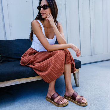 Vista Hi 2 brown platform sandals with toes facing toward the camera on a seated woman