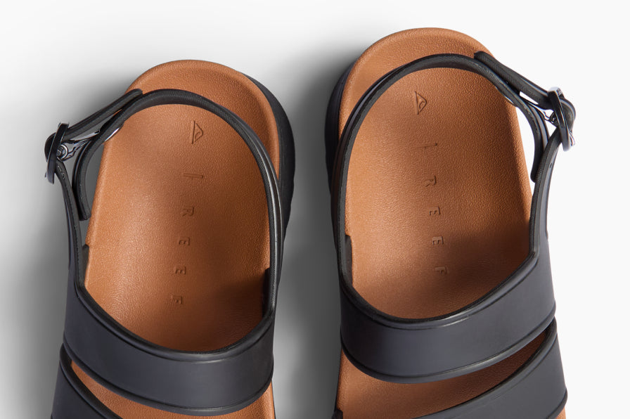 Top-down view of black sandals facing downward, showing brown cushioned footbeds and adjustable straps