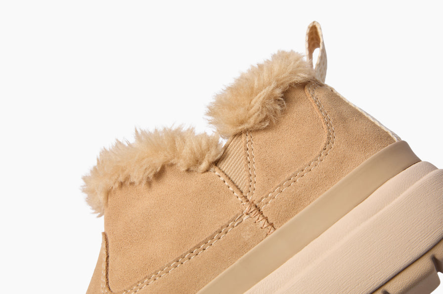 Close-up side view of a tan boot facing left, showing its fur-lined ankle collar and stitched upper