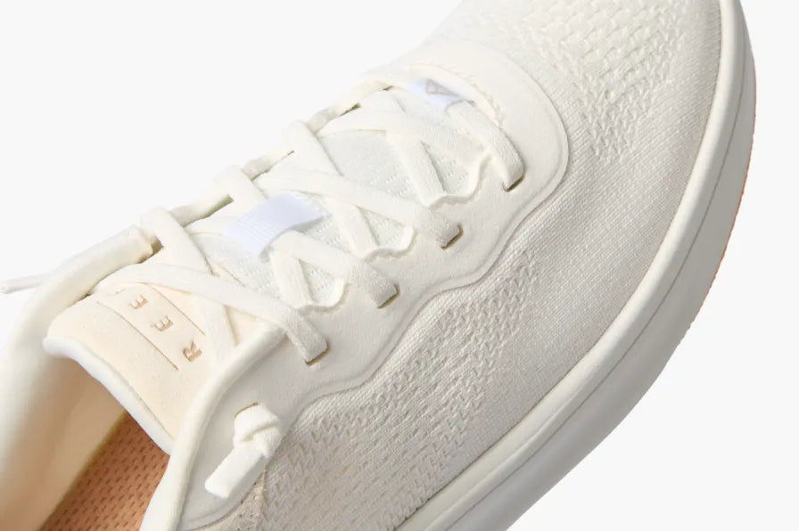 Close-up of the top and right side of a white sneaker facing right with textured knit upper and cushioned sole.