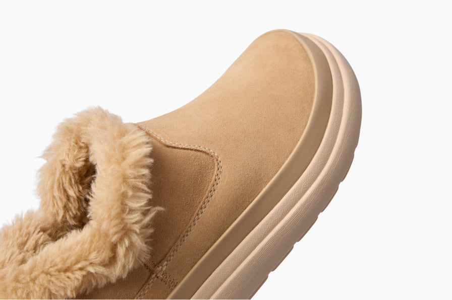 Close-up of a tan slip-on shoe facing right, with plush fur lining and a cushioned sole