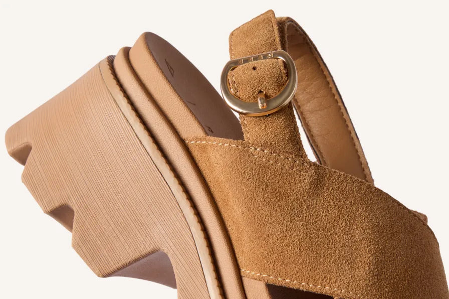 Close-up of a tan platform sandal facing left, showing its textured upper, buckle strap, and lugged sole.