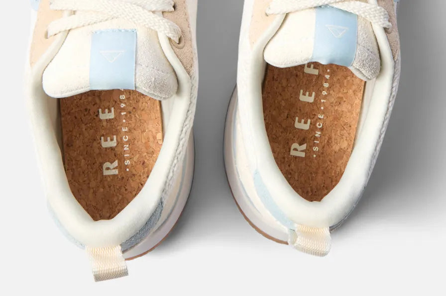 Top view of light beige and blue REEF sneakers showing cushioned collars and cork footbeds with branded insoles.