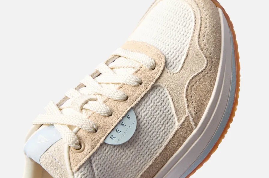 Close-up of the front and side of beige REEF sneaker with textured fabric, suede overlays, and white laces facing right