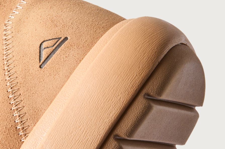 Close-up of tan suede footwear heel facing right, showing textured rubber sole and reinforced stitching detail