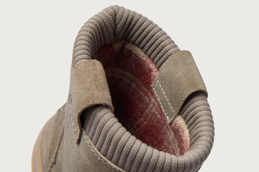 Close-up of a tan shoe facing upward, showing its ribbed collar, suede straps, and red fleece lining