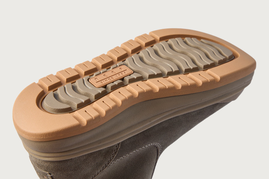 Close-up of a dark boot facing right, showing its tan outsole with rugged tread and wavy traction pattern