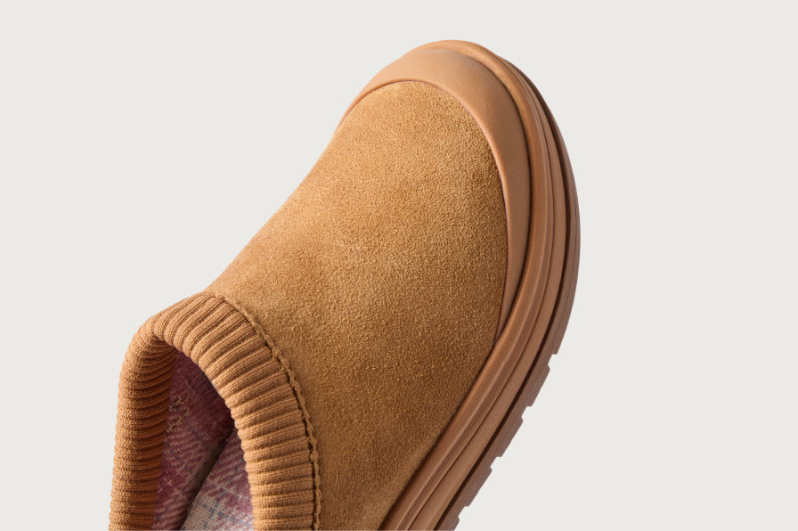 Close-up of a tan slip-on shoe facing upper right, showing its ribbed collar, soft upper, and layered sole