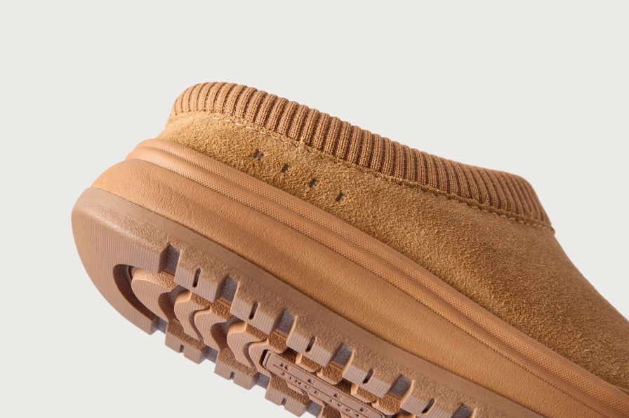 Tan slip on shoe facing left, close up of its textured outsole and ribbed collar