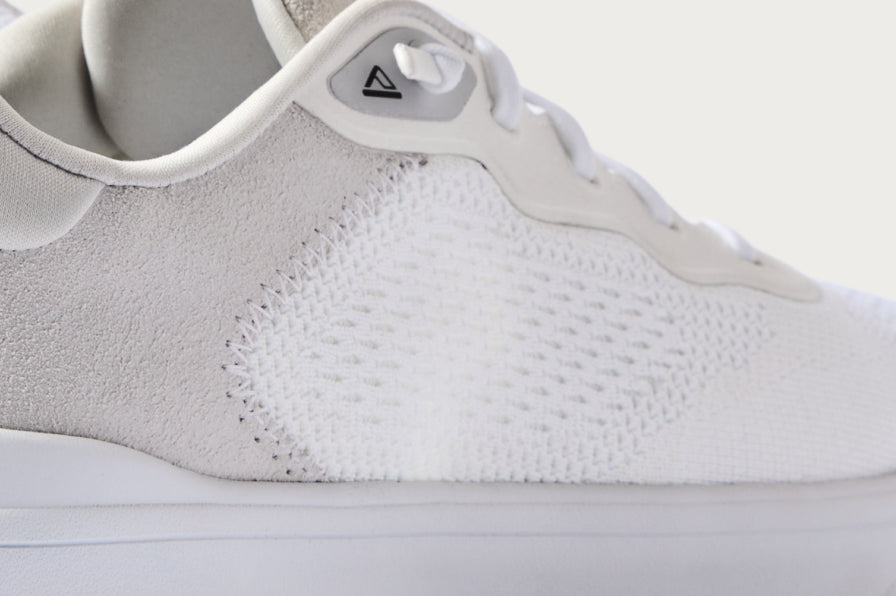 Close-up side view of a white sneaker facing right, showing its textured mesh upper and cushioned sole