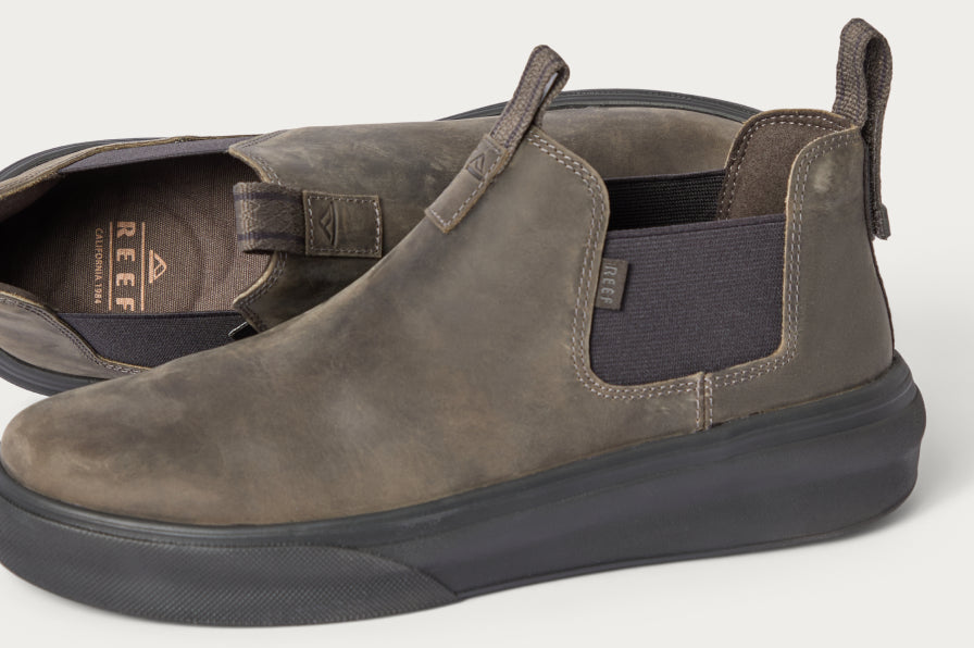 Pair of brown REEF slip-on shoes facing left with black elastic side panels and cushioned sole visible