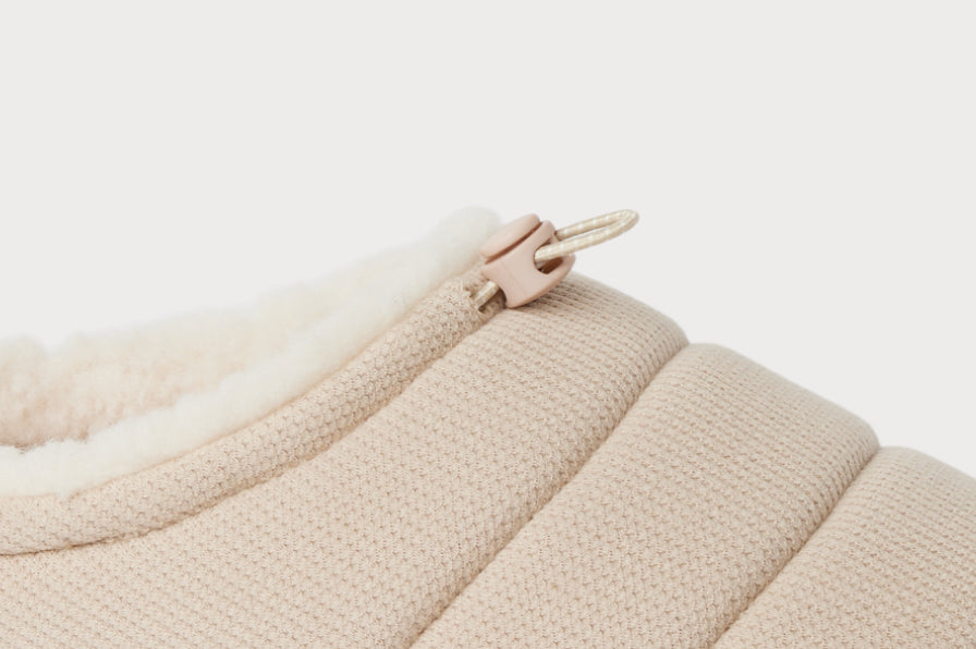 Close-up of the beige upper fabric and zipper pull on a slide shoe angled right with plush fleece lining for cozy comfort.