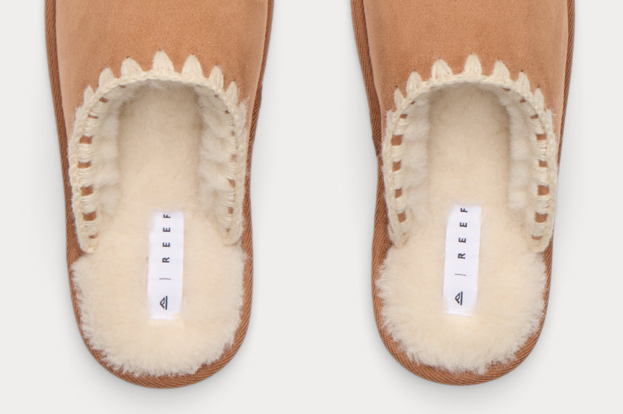 Top view of tan slip-on clogs with plush cream-colored lining and visible REEF tags for cushioned, beach-inspired comfort.