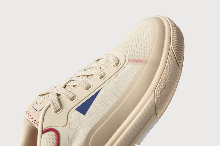 Close-up of a cream sneaker facing lower left, showing its laces, side panel, and textured sole