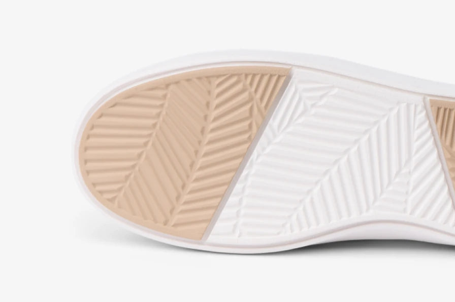 Close-up of a footwear outsole facing left, showing beige and white herringbone tread patterns for traction