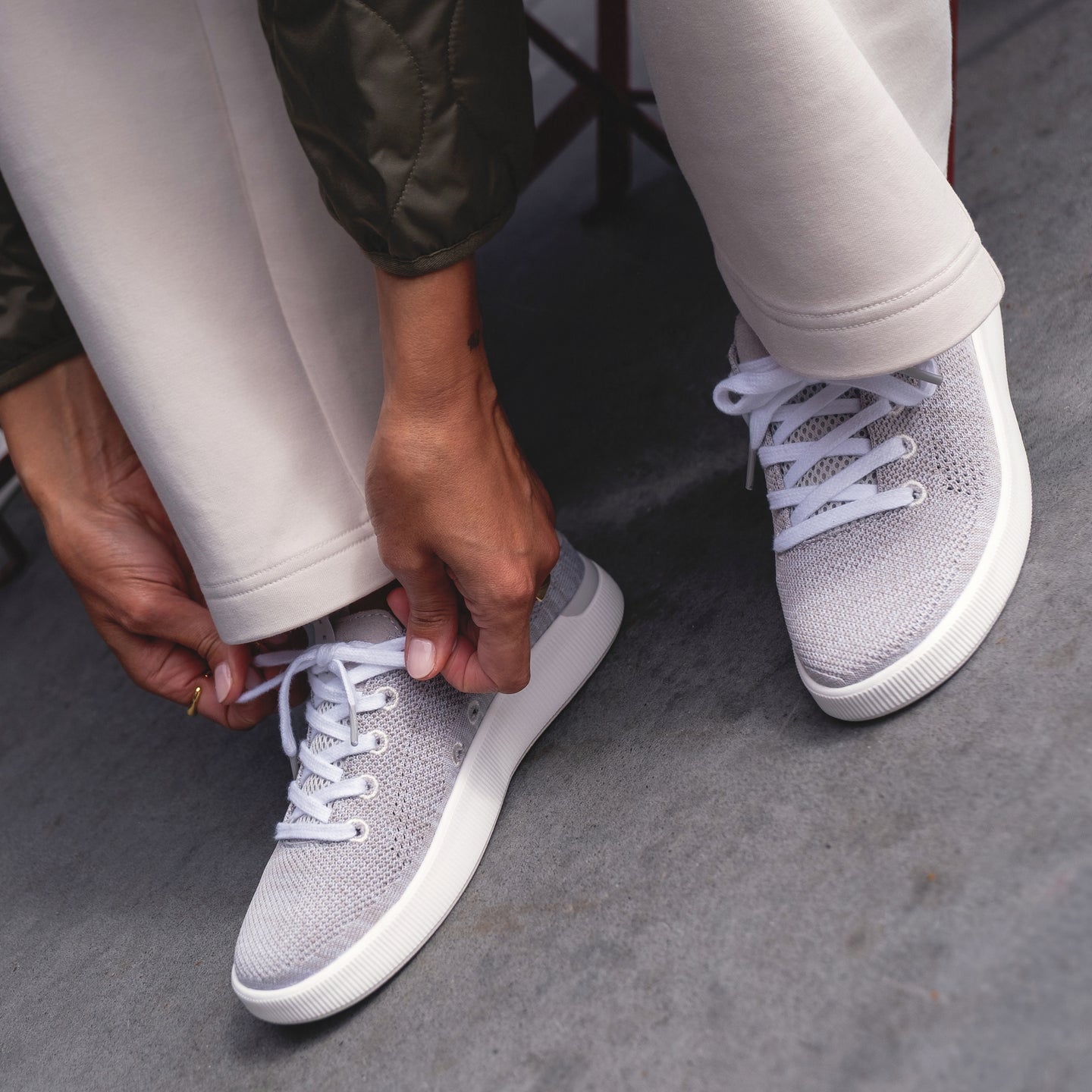 Person tying left-footed Reef Neptune sneaker facing forward, showing breathable stretch knit upper and cushioned sole.