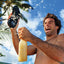 Man holding Fanning sandal facing up in beach setting with palm trees, showing sole and water splashing around him