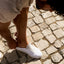 Neptune white sneaker facing right on cobblestone, close-up of man slipping foot in, highlighting comfort and beach-inspired design.