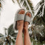 Sydnee Cutback Low - Sage - on a pair of feet up in the air with palm trees in the background