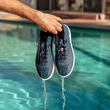 Hand holding a pair of navy Shoreline Del Mar H2O shoes facing forward, water draining from perforated toe area.