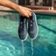 Hand holding a pair of navy Shoreline Del Mar H2O shoes facing forward, water draining from perforated toe area.