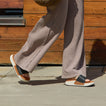 woman wearing Sydnee Cutback Low Black-Tan slide with long pants and walking down the sidewalk