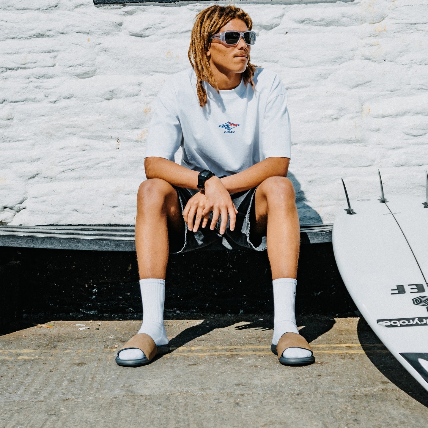 Tailslide men's tan slides with toes facing the camera on a seated model beside a surfboard