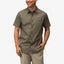 Man wearing olive green Topaz Shirt with subtle pattern and short sleeves, hands in pockets, smiling against white background