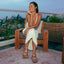 Woman sitting outdoors wearing Vista Luxe Liah sandals facing forward, showing top and straps with beach-inspired comfort design.