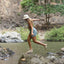 Woman wearing Reef Water Vista sandals facing right, mid-step over rocks by water, showing side view of sandals and arch support.
