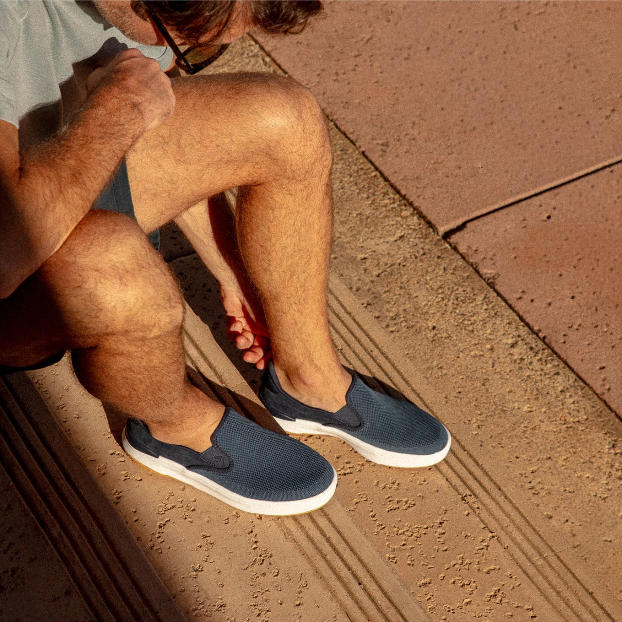 Del Mar Slip On facing right on model, men's navy slip-on sneaker with cushioned sole and lightweight design for beach-inspired comfort.
