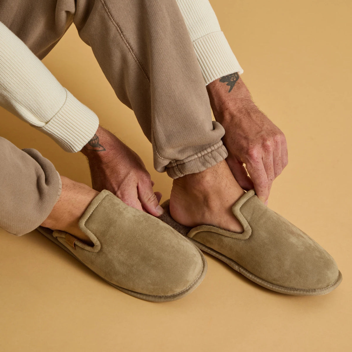 Close-up of beige slip-on clogs facing right as a person adjusts the heels