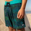 Close-up of the front and side of the Worley F/W Wvn Short with tropical print and teal waistband, beach setting.